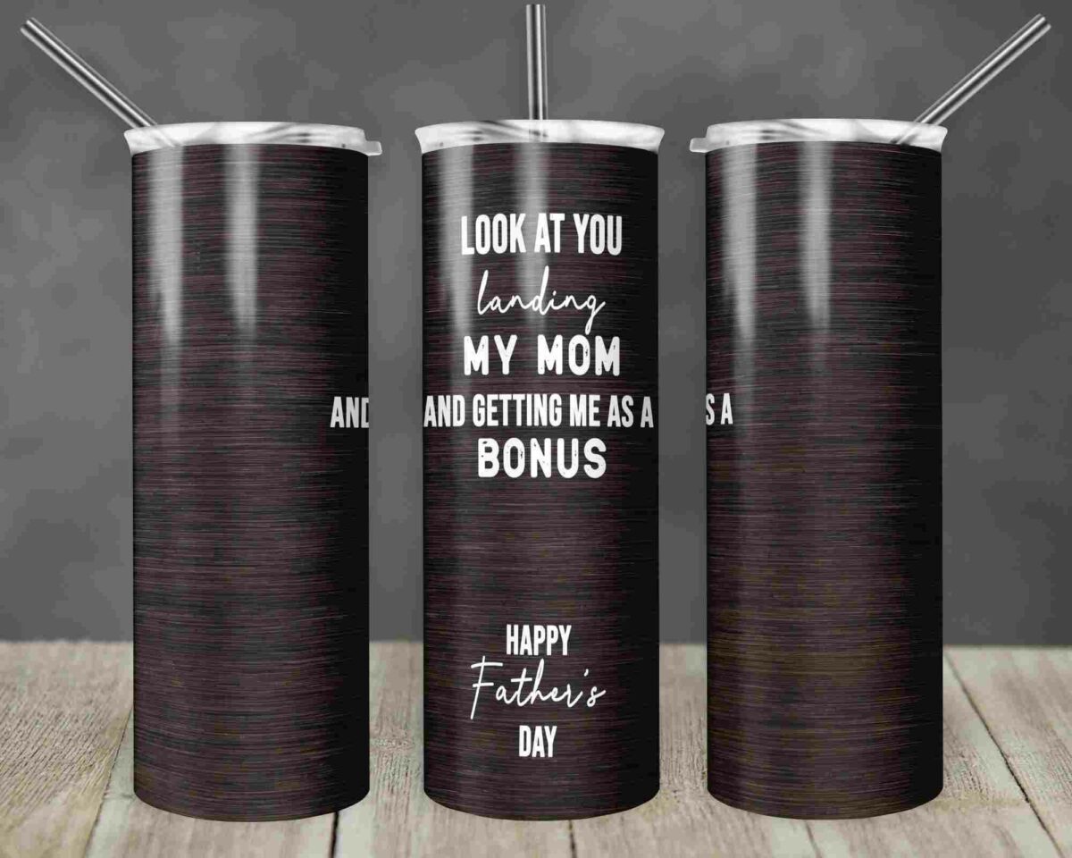 A dark wood-textured tumbler with a silver lid and straw is shown from three angles. The text on the tumbler reads, "Look at you landing my mom and getting me as a bonus. Happy Father's Day." The background is blurred and rustic.