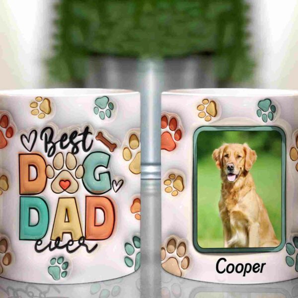 Two mugs are shown. One says "Best Dog Dad Ever" with colorful paw prints and bones; the other features a photo of a dog labeled "Cooper" with paw prints and bones surrounding the picture.