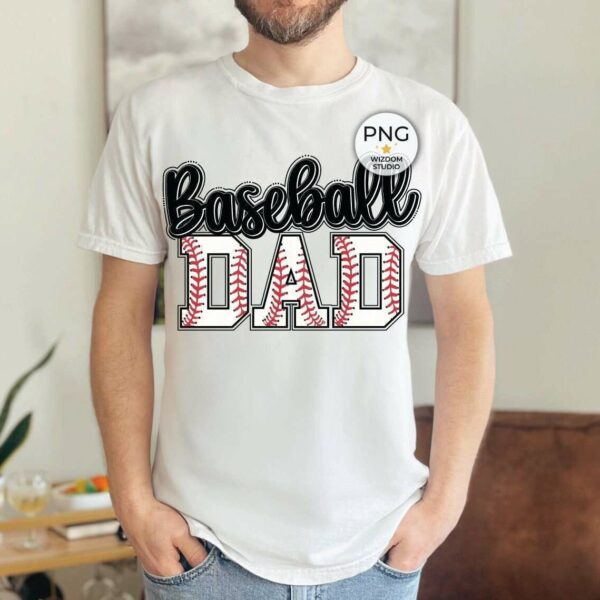 A person wearing a white t-shirt that reads "Baseball Dad" stands indoors. In the background, there's a plant on a table and a brown chair.