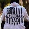 Person wearing a hoodie with an American flag and a baseball design, along with the text "BASEBALL DAD" on the back.