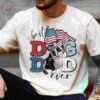 A person wears a light-colored T-shirt with a graphic of a dog and American flag, accompanied by the text "Best Dog Dad Ever.
