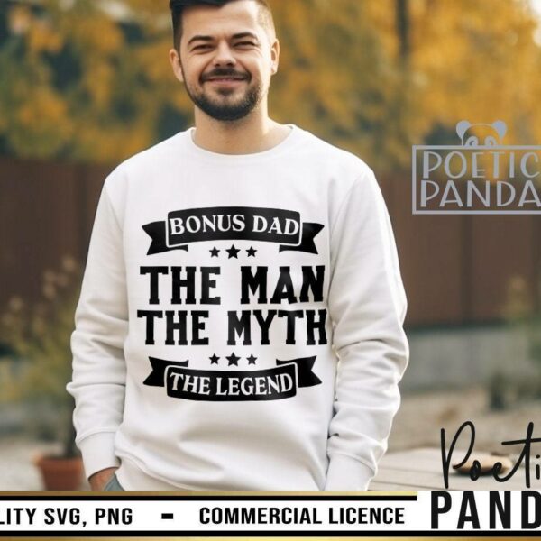 Alt Text: A man is wearing a white sweatshirt with the text "BONUS DAD, THE MAN, THE MYTH, THE LEGEND" in bold, black font. The background features an outdoor setting with greenery.