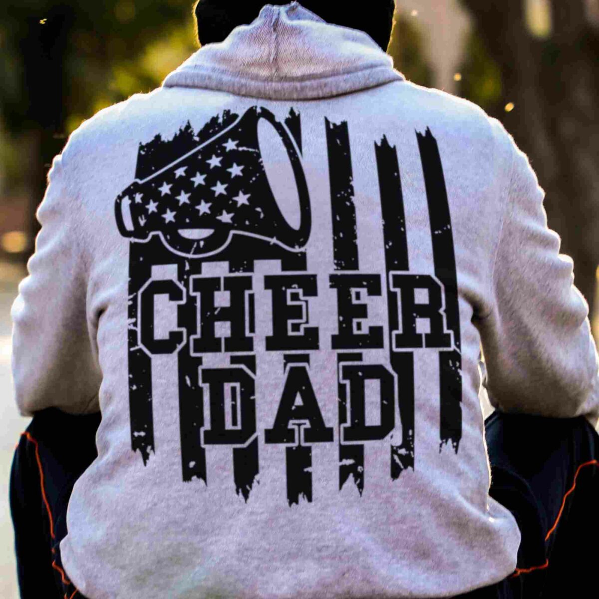 A person is wearing a hoodie with the text "CHEER DAD" and a megaphone graphic on the back.