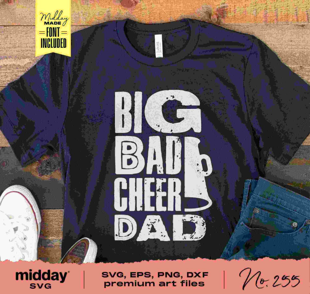 A black T-shirt lays flat on a wooden surface alongside a pair of rolled-up jeans and white sneakers. The shirt features the phrase "BIG BAD CHEER DAD" in bold white letters with a cheer megaphone graphic integrated into the design.