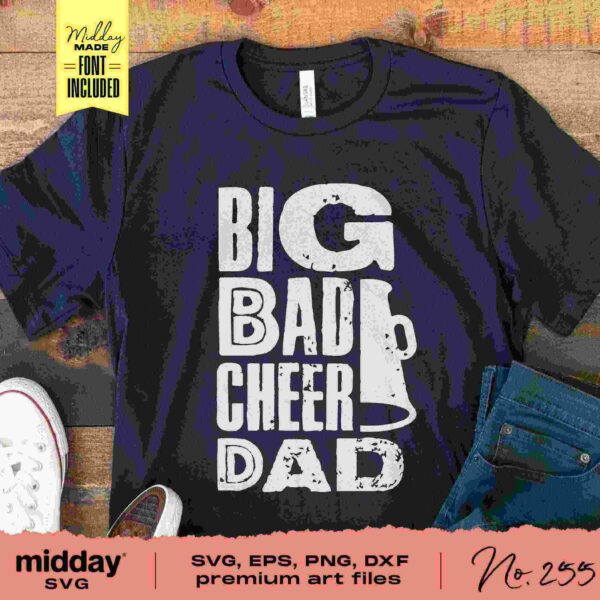 A black T-shirt lays flat on a wooden surface alongside a pair of rolled-up jeans and white sneakers. The shirt features the phrase "BIG BAD CHEER DAD" in bold white letters with a cheer megaphone graphic integrated into the design.