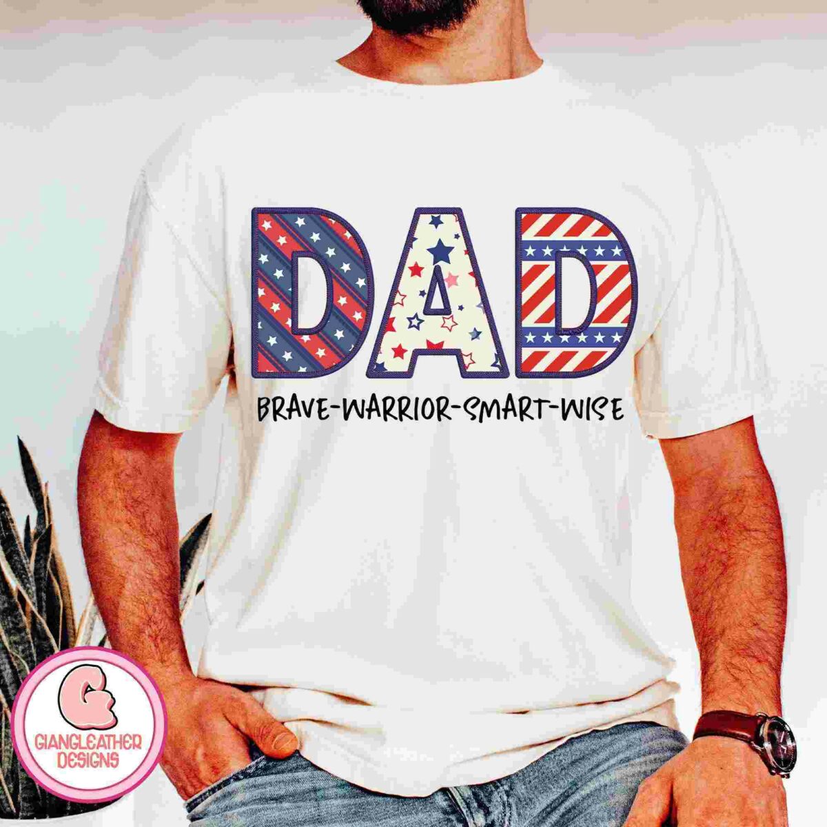 A person wears a white t-shirt with the word "DAD" in bold, patriotic stars and stripes design. Below, it reads "BRAVE-WARRIOR-SMART-WISE." The shirt also bears a small logo that reads "GIANGLEATHER DESIGNS.