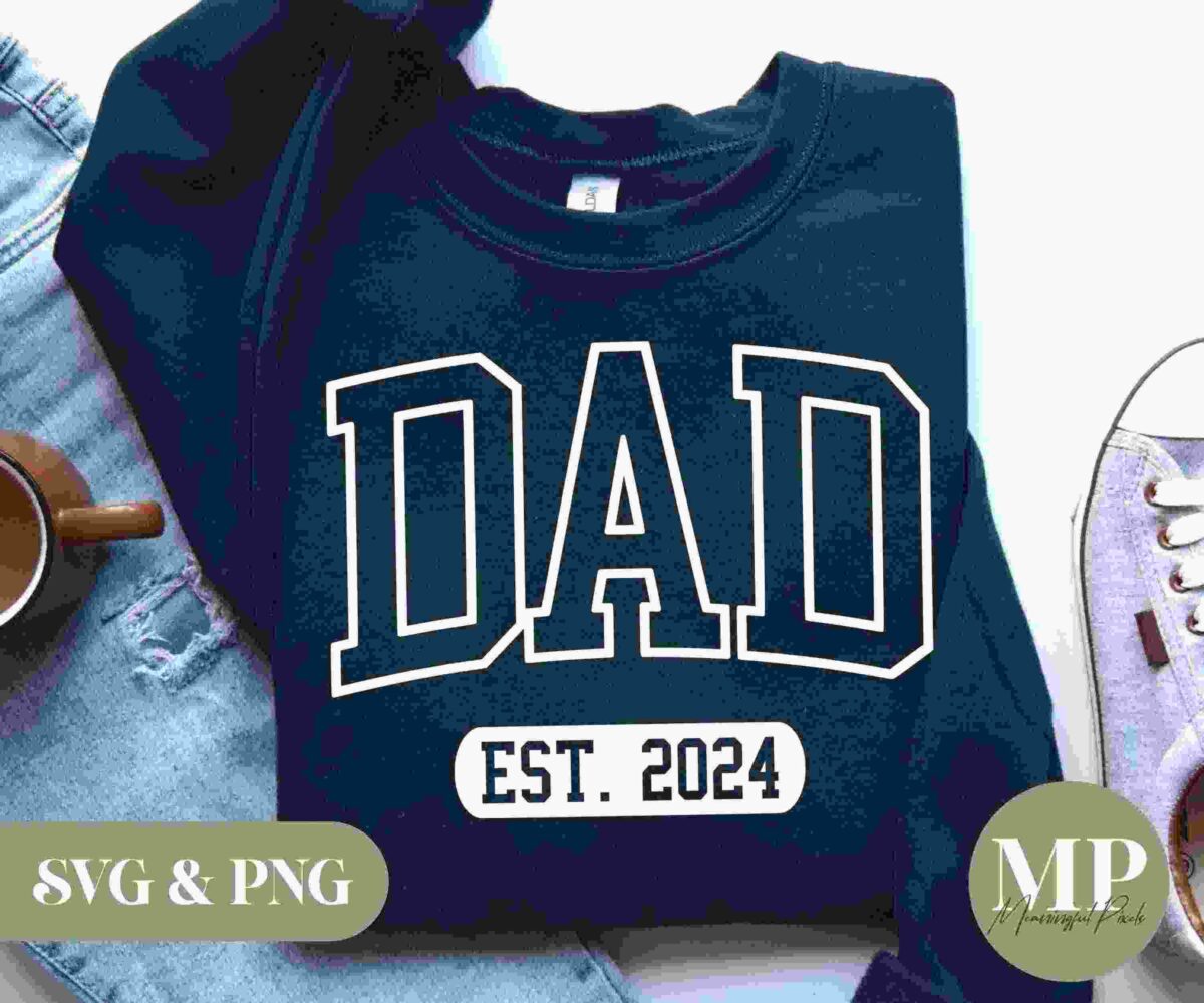 Navy blue sweatshirt with the word "DAD" and "EST. 2024" printed in white on the front, laid on light blue jeans next to a brown mug and sneakers. Text overlay reads "SVG & PNG" and "MP Moving Press".