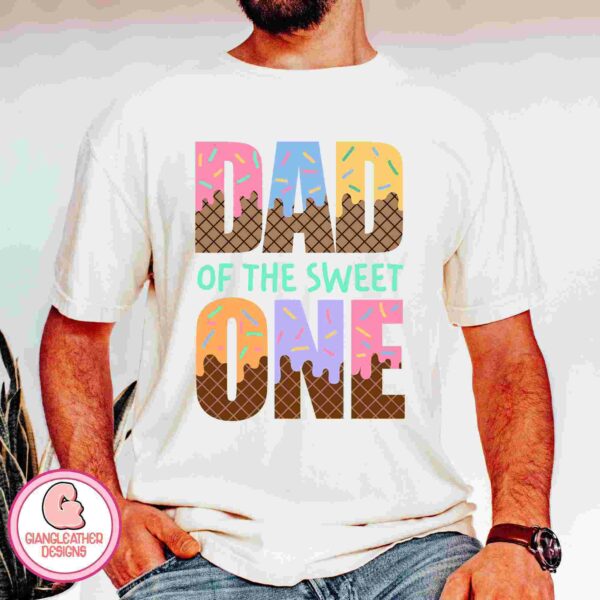 A person wearing a white t-shirt with colorful text that reads "DAD OF THE SWEET ONE." The shirt features ice cream-themed designs within the letters.