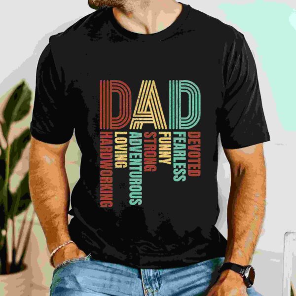 A person wearing a black T-shirt with the word "DAD" in large colorful letters, followed by various descriptive words such as "loving", "hardworking", "adventurous", and others.