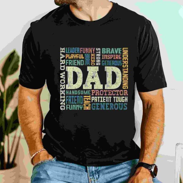 Alt Text: A man is wearing a black t-shirt that displays various words describing a dad, such as leader, brave, protector, understanding, and generous, arranged creatively around the word "DAD" in the center.