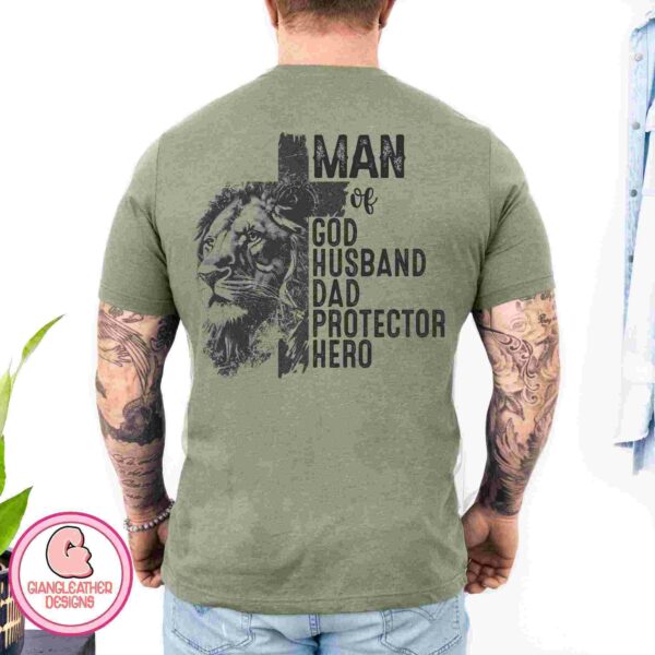 A man wearing a green T-shirt with a lion graphic and the text "MAN of GOD HUSBAND DAD PROTECTOR HERO" on the back. He has tattoos on both arms and is standing with his back to the camera. The background has a logo that says "GIANGLEATHER DESIGNS.