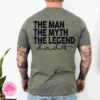 A person with tattoos is wearing a green t-shirt with the text "The man, the myth, the legend, dad" printed on the back.