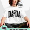 A person with long curly hair wearing a white t-shirt with the text "DADA" in a bold, checkered design sits against a plain background. The t-shirt branding reads "The Cosmic Studio Shop.