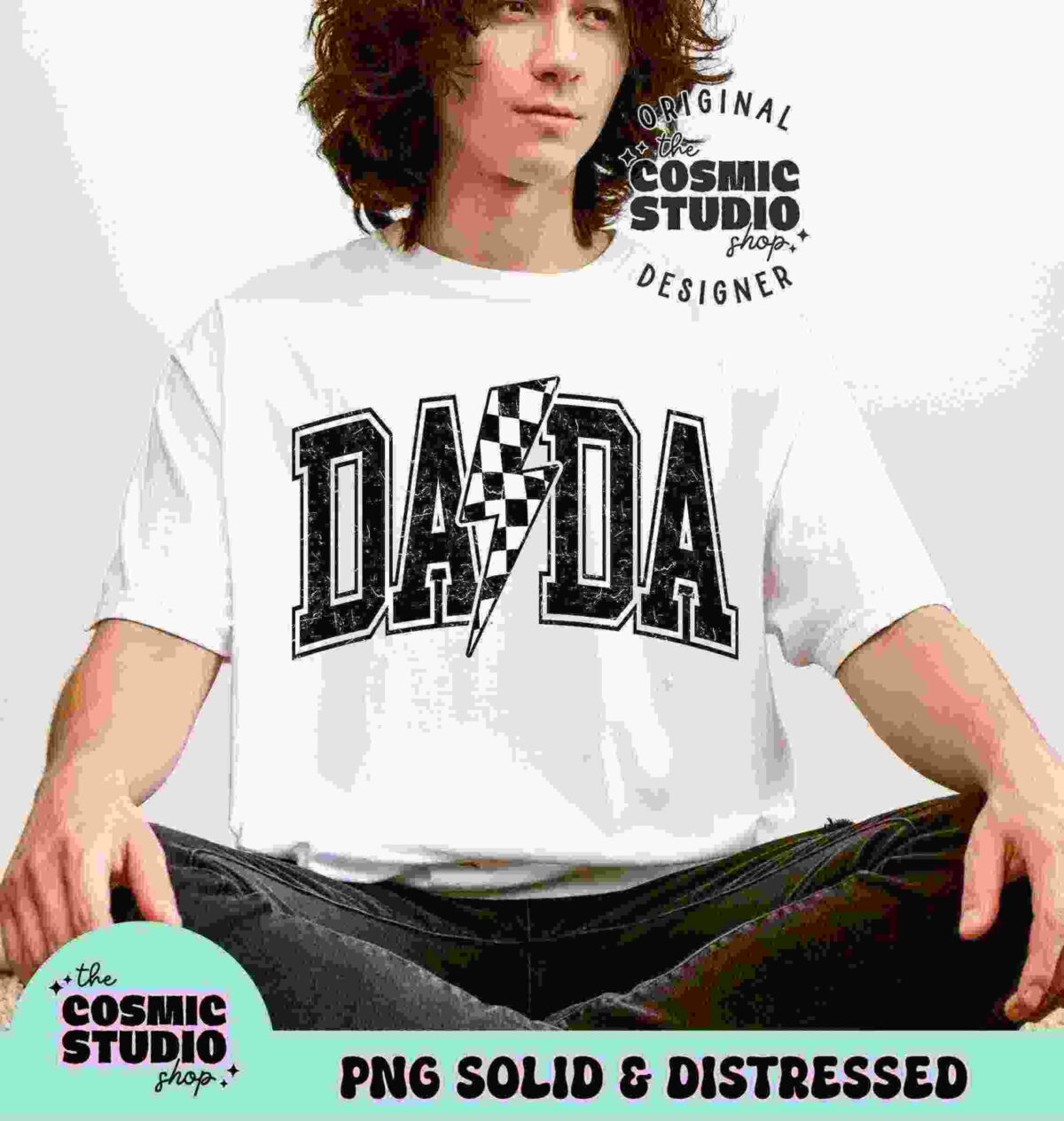 A person with long curly hair wearing a white t-shirt with the text "DADA" in a bold, checkered design sits against a plain background. The t-shirt branding reads "The Cosmic Studio Shop.