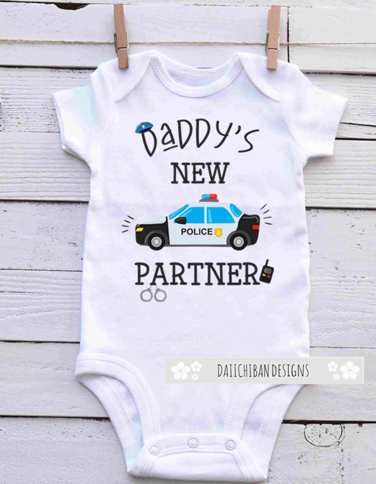 A white baby onesie with the text "Daddy's New Partner" featuring a graphic of a police car, a police hat, handcuffs, and a walkie-talkie.