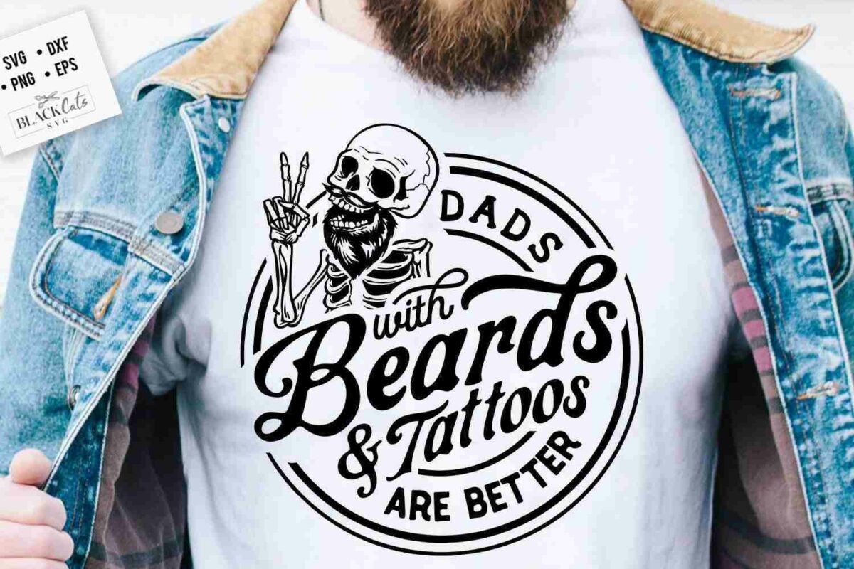 A person wearing a denim jacket and a white T-shirt displaying a skeleton with tattoos and the text "Dads with Beards & Tattoos Are Better.