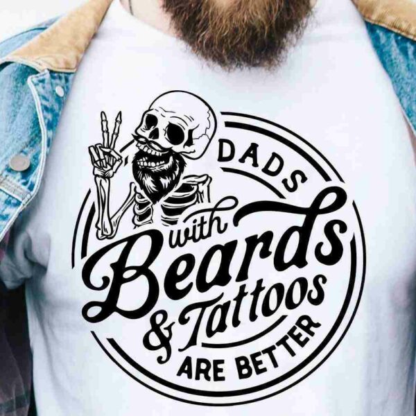 A person wearing a denim jacket and a white T-shirt displaying a skeleton with tattoos and the text "Dads with Beards & Tattoos Are Better.