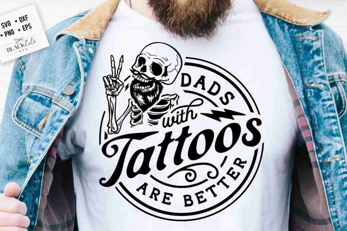 A person wearing a denim jacket and a white t-shirt with a graphic of a skeleton making a hand gesture, accompanied by the text "Dads with Tattoos Are Better.