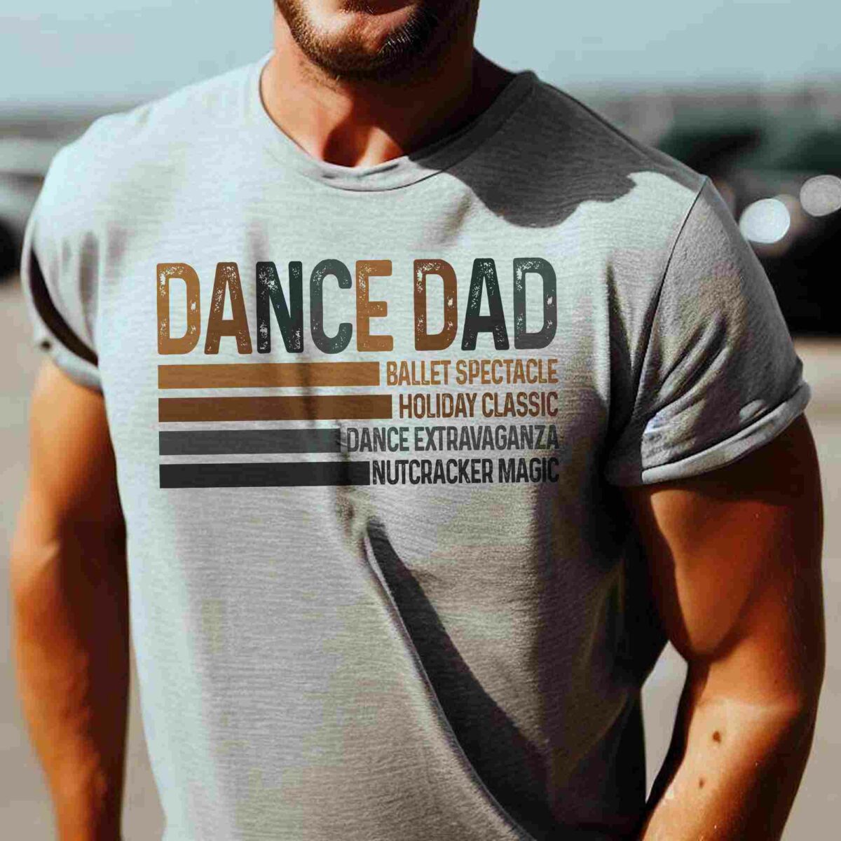 A person wearing a light gray T-shirt that reads "DANCE DAD" followed by "Ballet Spectacle, Holiday Classic, Dance Extravaganza, Nutcracker Magic" in smaller text below.