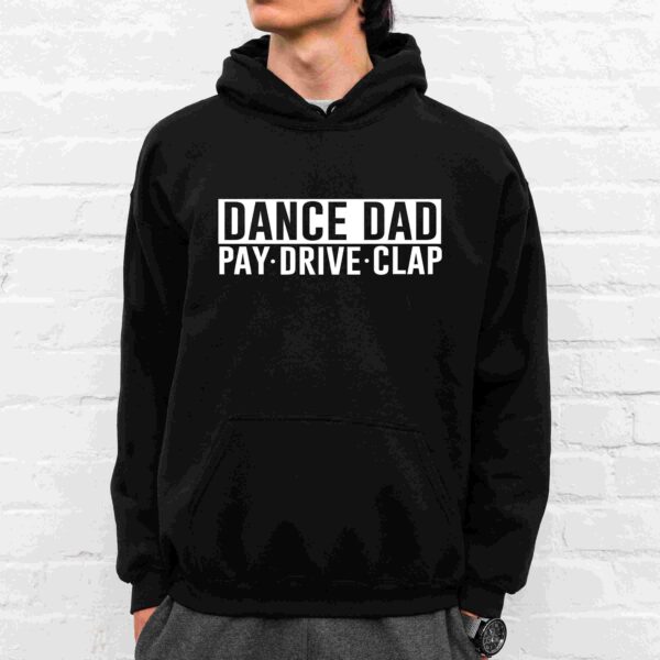 A person wearing a black hoodie with the text "DANCE DAD PAY· DRIVE· CLAP" printed on the front, standing in front of a white brick wall.