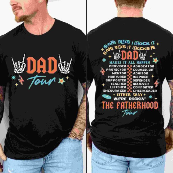 A man wearing a black t-shirt with two designs. The front shows skeletal hands making a rock gesture with the text "Dad Tour." The back lists various dad roles like "Provider," "Mentor," "Friend," and "Teacher" under the words "Dad Tour" and "The Fatherhood Tour.