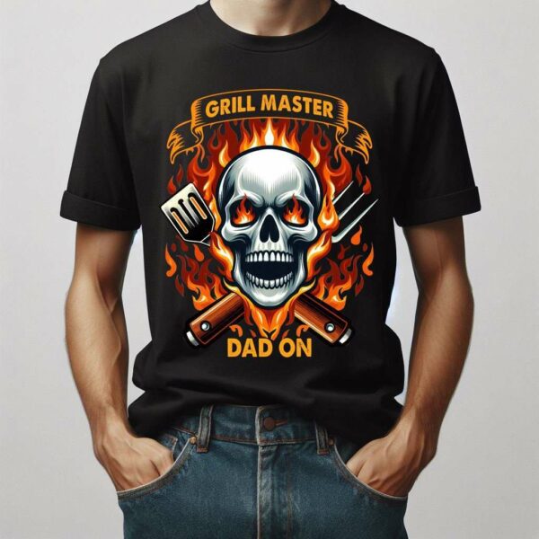 Person wearing a black T-shirt with a flaming skull design, crossed grilling tools, and the text "Grill Master Dad On.