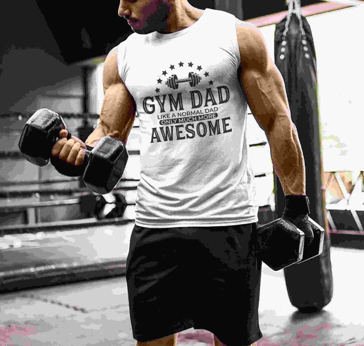 A man in a gym setting, wearing a sleeveless shirt that reads "Gym Dad: Like a Normal Dad Only Much More Awesome," and holding dumbbells in each hand.