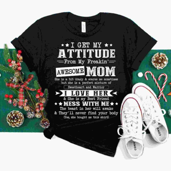 Black t-shirt with white text saying: "I get my attitude from my freakin' awesome mom. She is a bit crazy & scares me sometimes but she is a perfect mixture of sweetheart & warrior." Surrounded by holiday decorations.