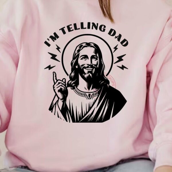 A person is wearing a pink sweatshirt featuring an illustration of Jesus with the text "I'm Telling Dad" and lightning bolts around the text.