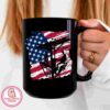 Person holding a black mug featuring an American flag background with a silhouette of someone sitting on a ski lift.