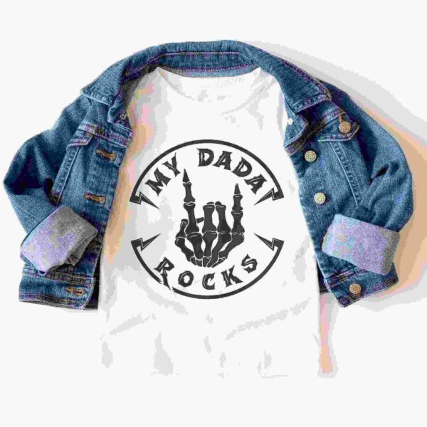 A white t-shirt with a skeleton hand graphic and the text "MY DADA ROCKS" is displayed under a blue denim jacket with rolled-up sleeves.