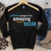 A black sweatshirt with the text "prime example of an amazing mom" displayed on a bed with leopard print fabric, blue jeans, a leather belt, and a pair of brown boots.