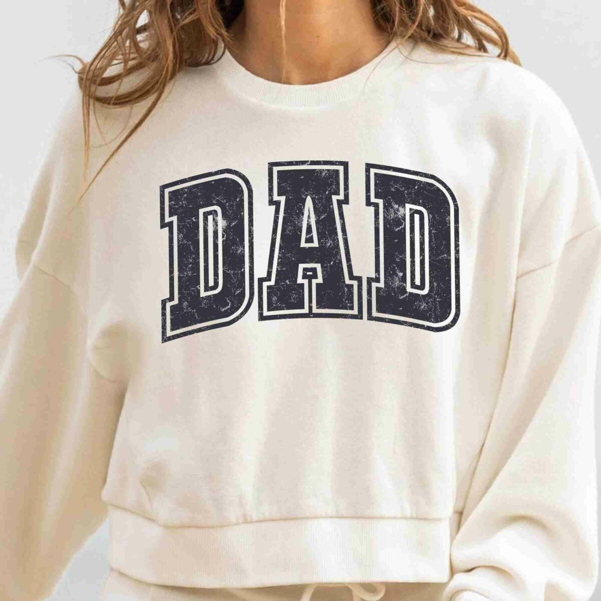 Person wearing a white sweatshirt with the word "DAD" printed in large, bold, distressed letters on the front.