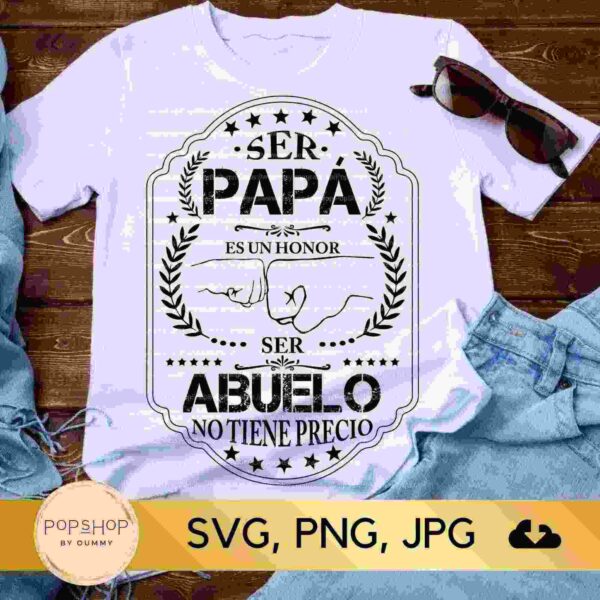 White t-shirt with Spanish text "Ser papá es un honor, ser abuelo no tiene precio" meaning "Being a dad is an honor, being a grandfather is priceless," laid beside sunglasses and denim shorts.