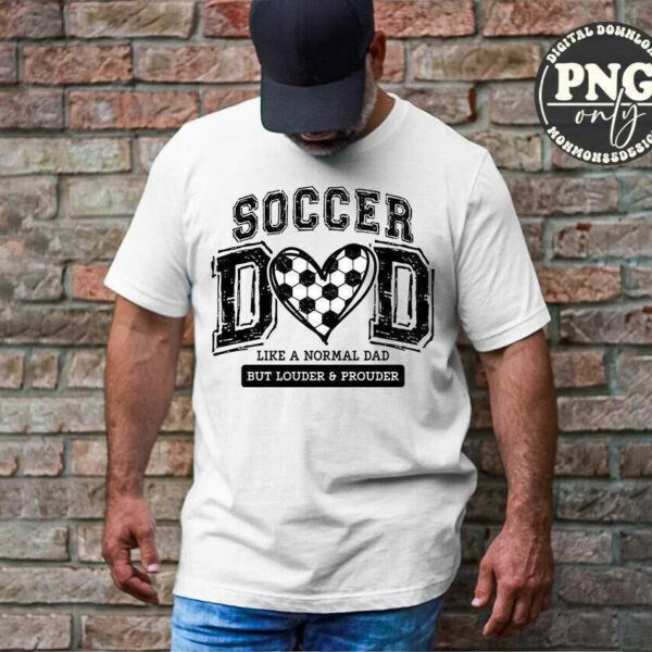 A man in a baseball cap stands against a brick wall wearing a white T-shirt that reads "Soccer Dad: Like a normal dad but louder and prouder.