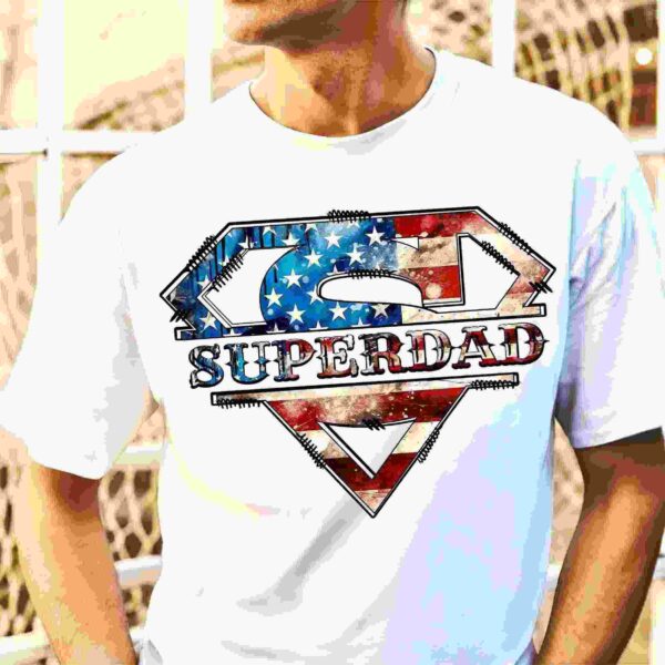 Man wearing a white t-shirt with an illustrated "Superdad" logo, designed in a style reminiscent of the Superman emblem, embellished with the American flag's stars and stripes.