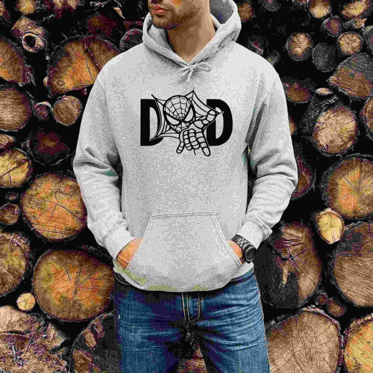 A person wearing a gray hoodie with a spiderweb design and the letters "DAD" stands in front of a stack of cut logs.