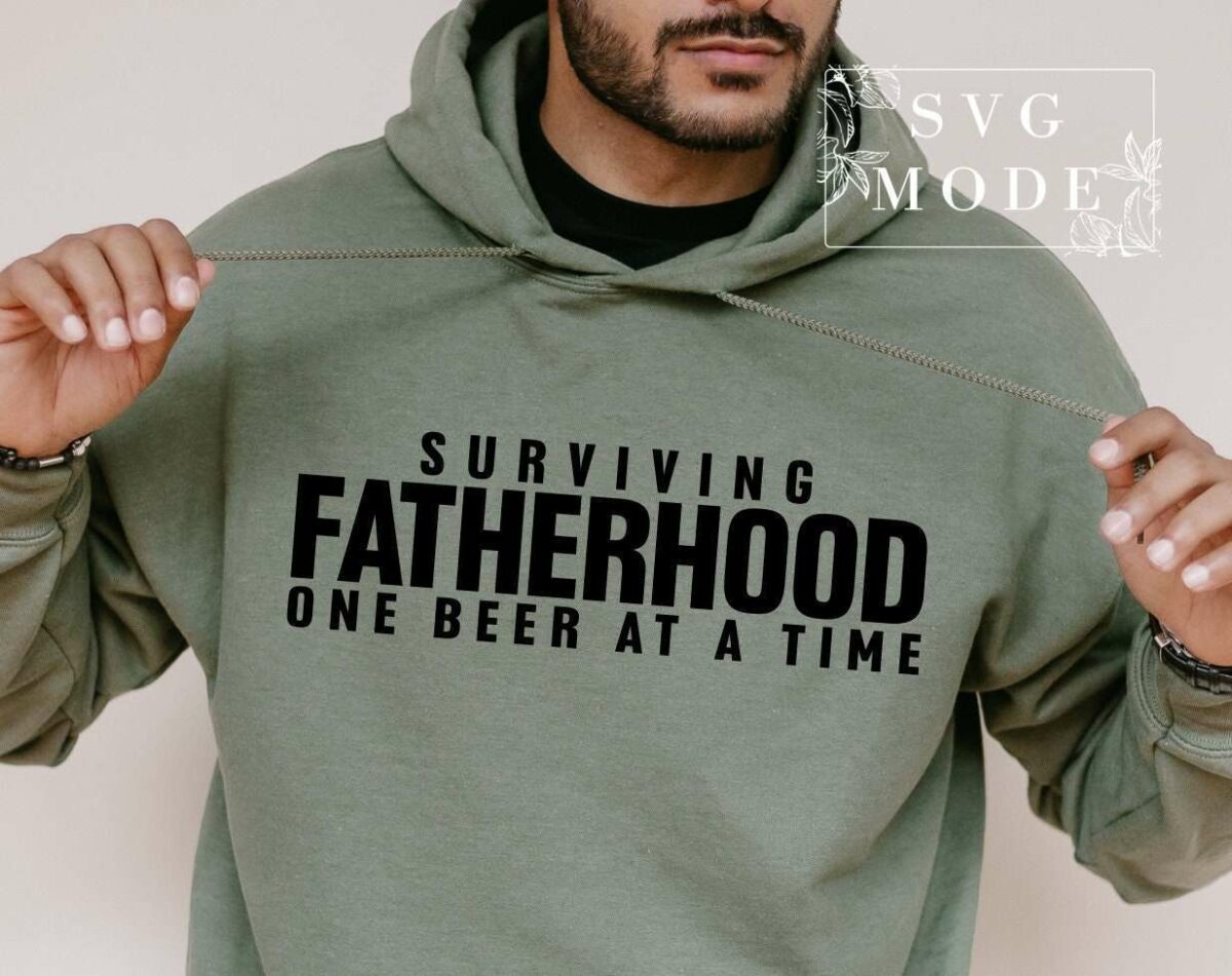 A man wears a green hoodie with the text "Surviving Fatherhood One Beer at a Time." The image includes a watermark that reads "SVG Mode.