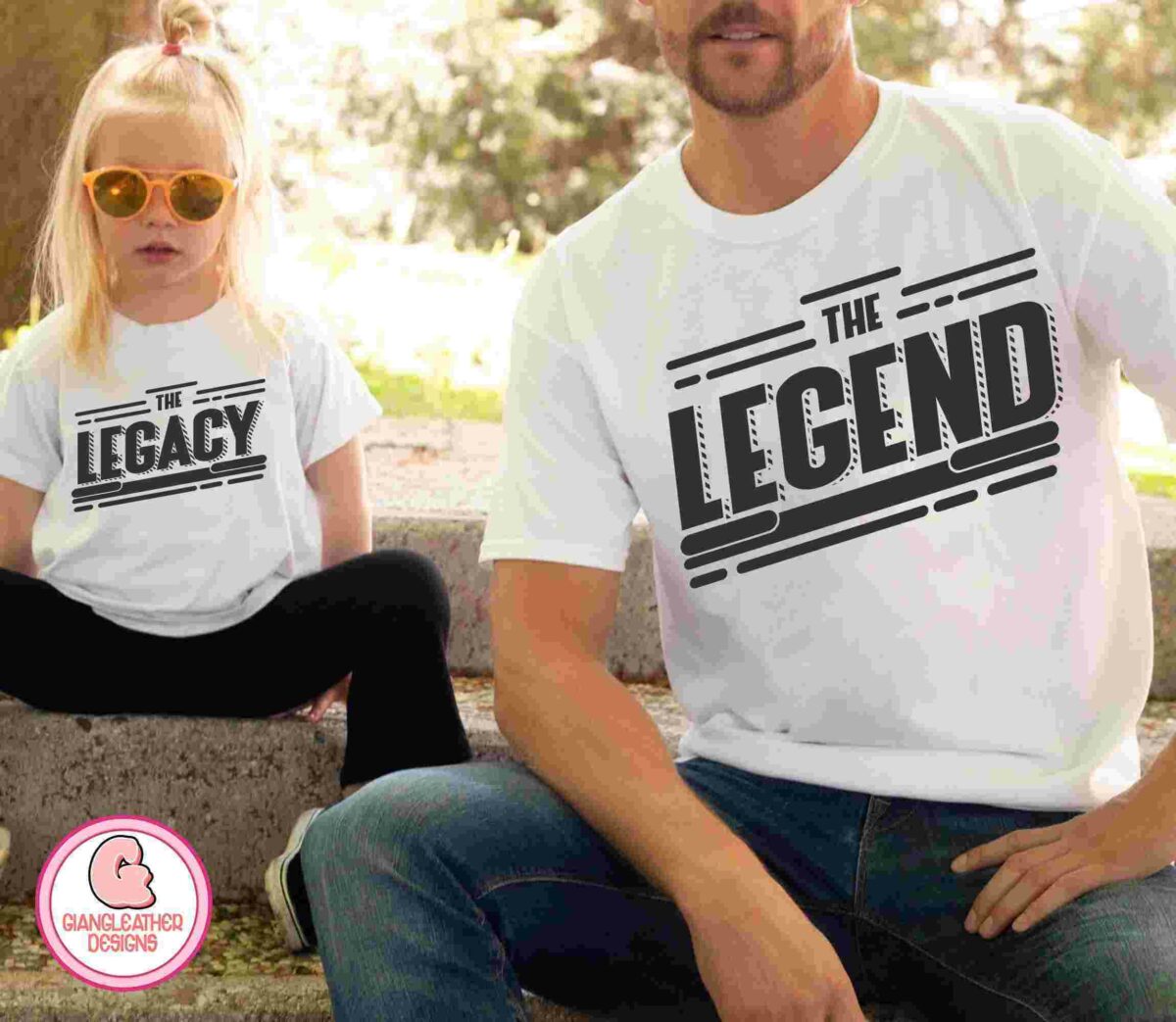 A child wearing a "The Legacy" t-shirt sits next to an adult wearing a "The Legend" t-shirt. They are sitting outside on a stone bench.