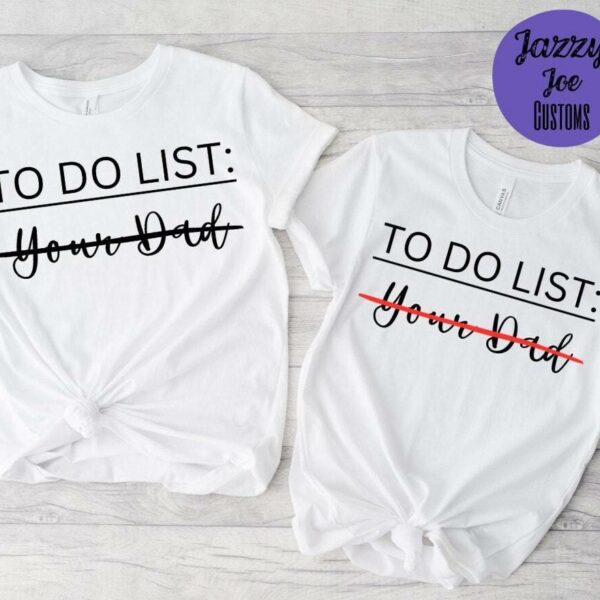 Alt Text: Two white T-shirts from Jazzy Joe Customs on a light wooden surface. Both have "TO DO LIST: Your Dad" with "Your Dad" crossed out. Both shirts are tied in a front knot.