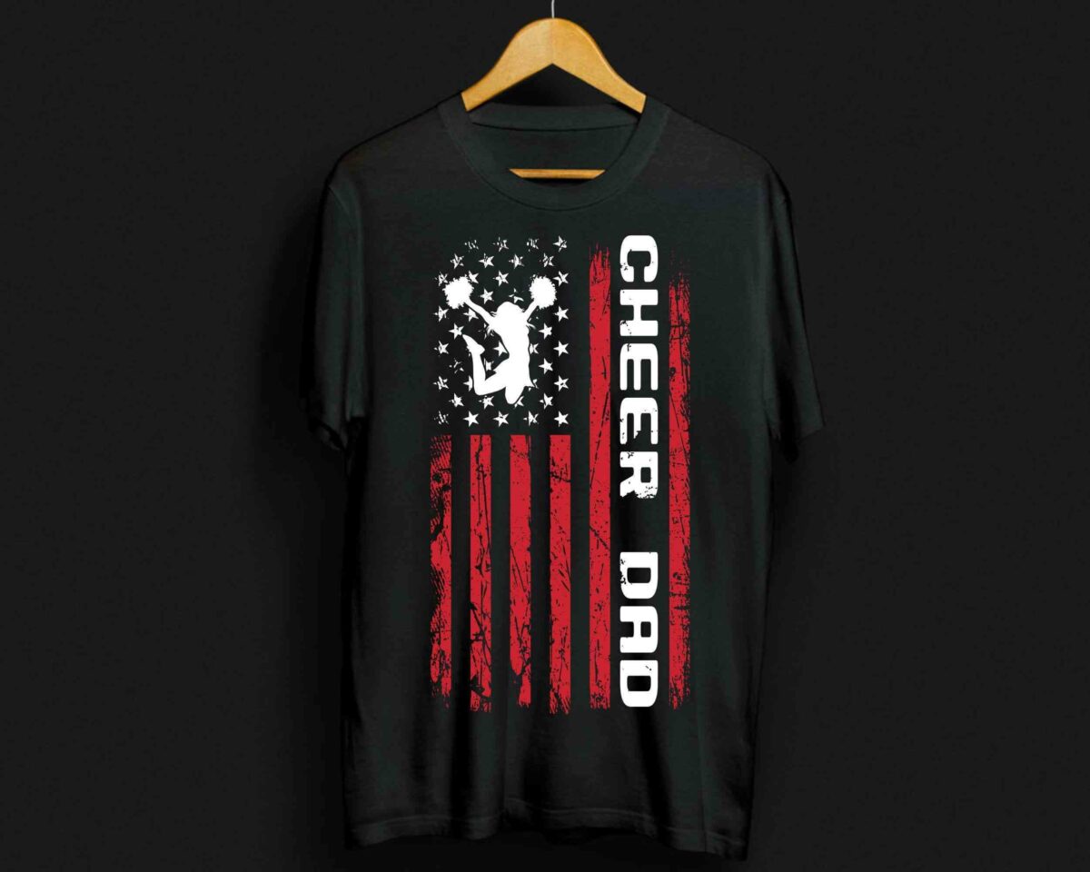 Black T-shirt with “CHEER DAD” text and graphic displaying a cheerleader silhouette over a distressed American flag design in white and red. The shirt is displayed on a wooden hanger.