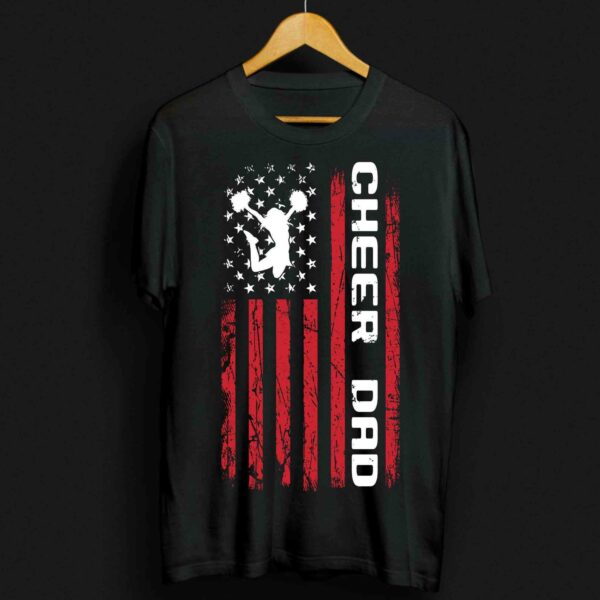 Black T-shirt with “CHEER DAD” text and graphic displaying a cheerleader silhouette over a distressed American flag design in white and red. The shirt is displayed on a wooden hanger.