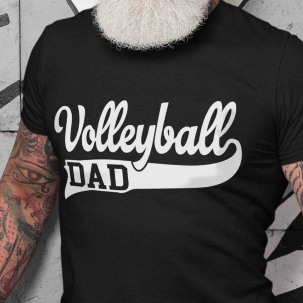 A person with a white beard and tattooed arms is wearing a black T-shirt that says "Volleyball Dad" in white lettering.