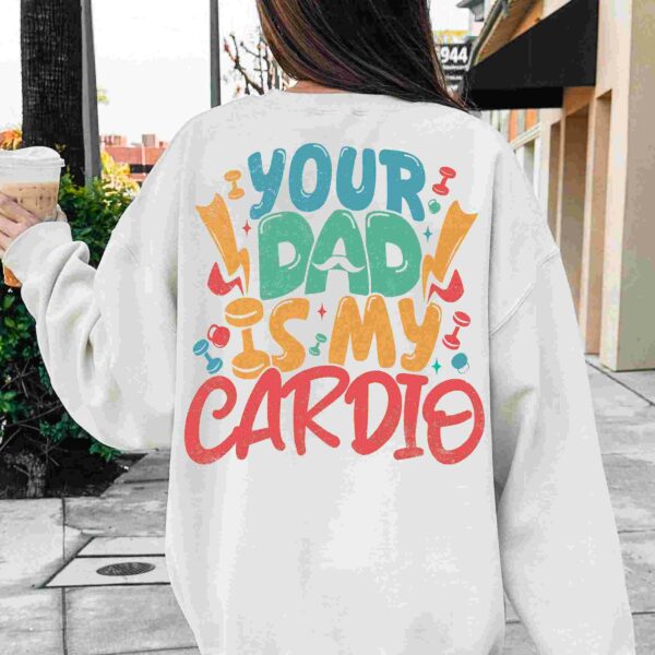 Person wearing a white sweatshirt with colorful text on the back that reads "Your Dad is My Cardio," holding a cup of iced coffee while walking on a sidewalk.